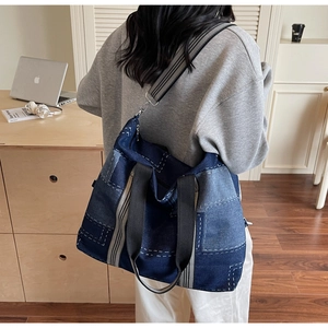 Detail of a large denim patchwork tote bag with contrast stitching and striped strap