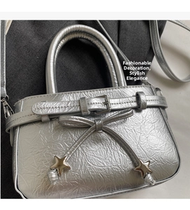 Detail of silver metallic leather handbag featuring bow, star charms, and pleated texture