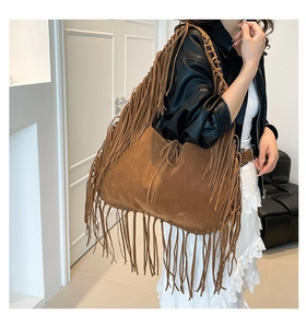 Detail of a large brown suede tote bag with fringe accents and a braided shoulder strap