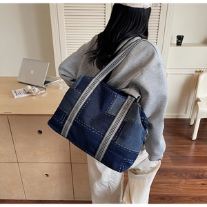 Detail of a patchwork denim tote bag with decorative stitching and striped strap