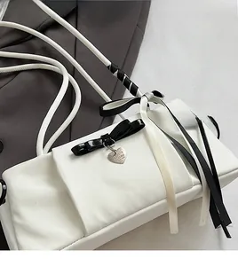 Detail of white fabric shoulder bag with black bow, ribbons and heart-shaped pendant