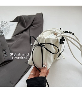 Close-up of white pleated leather shoulder bag with decorative black ribbon bow and zipper