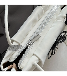 Close-up of smooth silver zipper on a white leather shoulder bag with a black bow charm