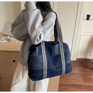 Detail of a large denim tote bag with gray woven straps and contrast stitching accents