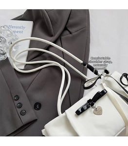 Detailed view of white leather shoulder bag with black bow and silver heart pendant detail