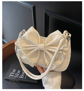 Detail of cream bow-shaped handbag with pearl strap and silver floral chain