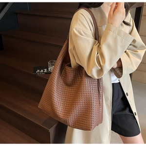 Detail of large brown woven tote bag showing premium texture on a shoulder strap model