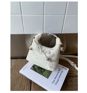 Gros plan du sac seau crème avec mini clous métalliques et détail de nœud élégant
