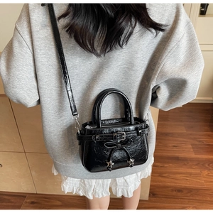 Detail of black patent leather mini bucket bag with star charms and bow on model
