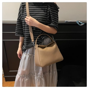 Detail of soft leather handbag in earth brown with wide shoulder strap worn by model
