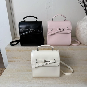 Three elegant leather handbags in black, pink and beige displayed on stone steps