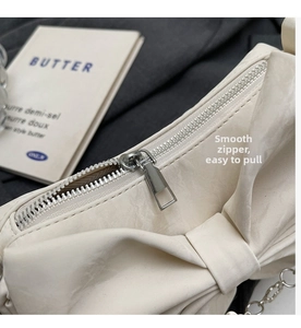 Macro detail of smooth silver-tone metal zipper on cream bow shoulder bag