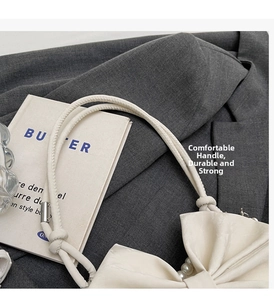 Close-up of cream bow shoulder bag with rope handle and pearl accents on gray blazer