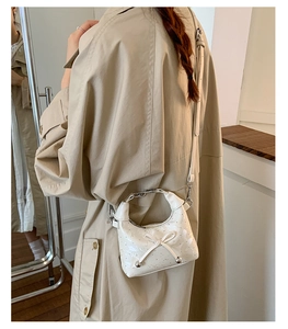 Detail of white glossy mini shoulder bag with bow decor and silver beads on model