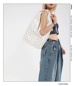 Gros plan d'un sac cabas en cuir verni blanc avec rivets argentés porté par un mannequin