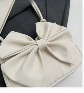 Detail of soft cream shoulder bag featuring large bow decor and elegant pearl accents