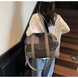 Detail view of large denim tote bag featuring gray patchwork design and striped handles