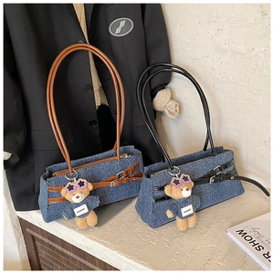 Detail of blue denim tote bags with leather straps and plush bear charm accents