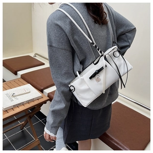 Detail of white shoulder bag featuring black bow accents and heart-shaped metal pendant