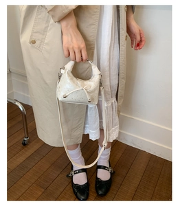 Close-up of white pleated crossbody bag featuring elegant bow detail and silver metal buckle