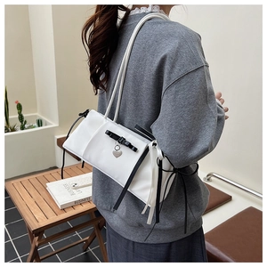Detailed view of white shoulder bag featuring black bow, heart charm, and long ribbons