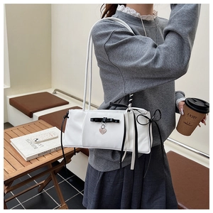 Close-up of white nylon shoulder bag with black bow, heart charm and long ribbons