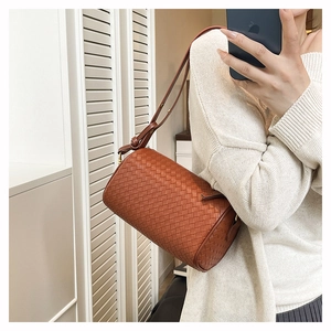 Detail of a brown woven cylindrical crossbody bag with crossbody strap and zipper closure