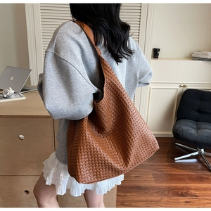 Detail of a large brown woven leather hobo bag worn as a shoulder bag on model