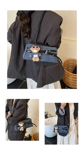 Detail view of denim shoulder bag with leather straps and a plush bear keychain ornament