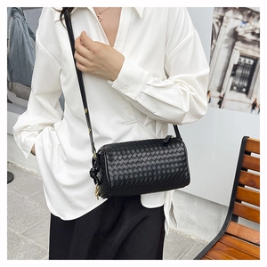 Detail of hand-woven black leather texture and gold hardware on a crossbody cylinder bag
