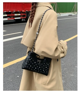 Detail of black quilted crossbody bag with silver studs and bow on a trench coat