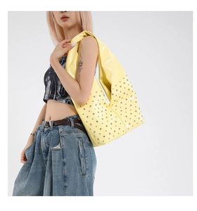 Vue détaillée du sac d'épaule en cuir verni jaune avec rivets sur le modèle