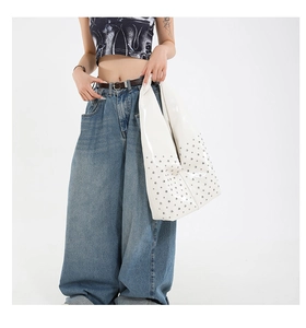 Détail d'un grand sac cabas blanc brillant avec des rivets argentés porté à l'épaule