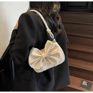 Detail of white bow shoulder bag featuring pearl and floral chain on black blazer