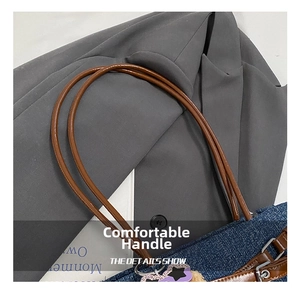 Detail of denim shoulder bag with brown leather handle and silver metal hardware accents