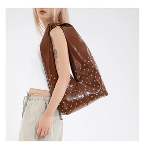 Close-up of brown glossy tote bag featuring silver rivet studs and pleated shoulder strap