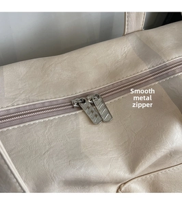Detail of smooth metal double zippers and lychee grain leather on cream tote bag