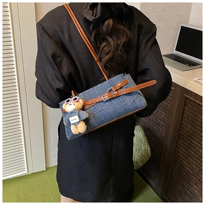 Detail of denim patchwork tote bag with brown leather strap and a cute bear bag charm
