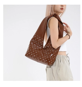 Détail d'un sac hobo en cuir marron avec des rivets argentés et une large bandoulière