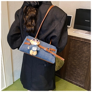 Model wearing blue denim shoulder bag with brown leather straps and plush bear charm