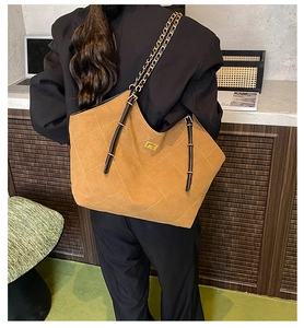 Close-up of khaki quilted tote bag featuring a gold turn-lock and metal chain strap