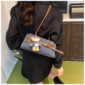 Detail of denim baguette bag with brown leather strap and teddy bear charm on model