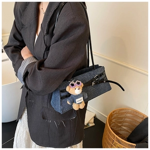 Detail of blue denim shoulder bag with cute teddy bear charm and black leather strap