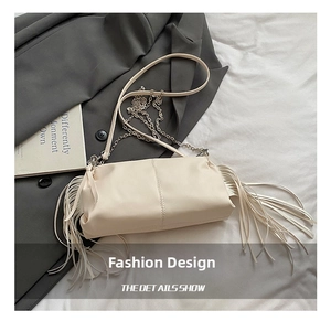 Detail van gebroken witte geplooide tas met lange franjes en elegante schakelketting