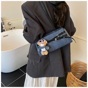 Blue denim underarm bag with black leather strap and a purple teddy bear charm detail