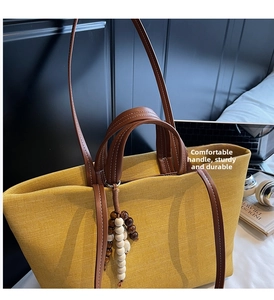 Detail of yellow canvas tote bag with brown leather handles and wooden bead charm