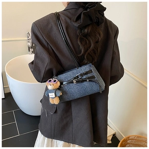 Detail of denim blue underarm bag with teddy bear pendant and black leather straps