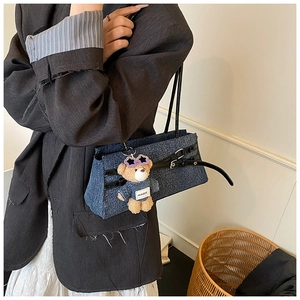 Detail of dark blue denim baguette bag with leather strap and plush bear charm