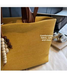 Detail of yellow canvas tote bag with brown leather handle and bead charm on white surface