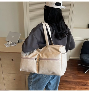 Detail of a large cream tote bag showing multiple zipper pockets and side compartments